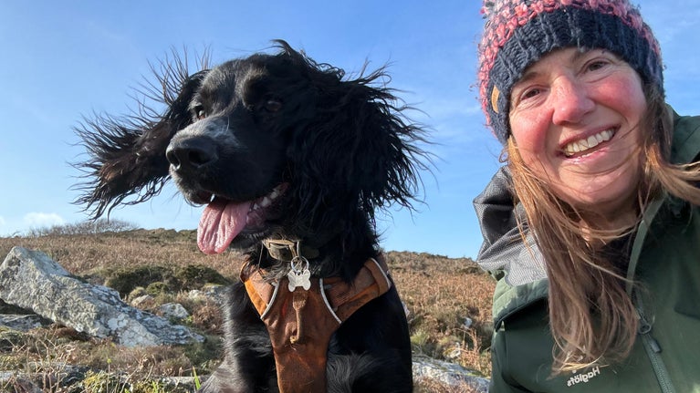 Lochy, a spaniel & her owner Vicki visiting Godolphin Hill. Lochy is wearing an orange harness & Vicki has on a woolly hat & green jacket.